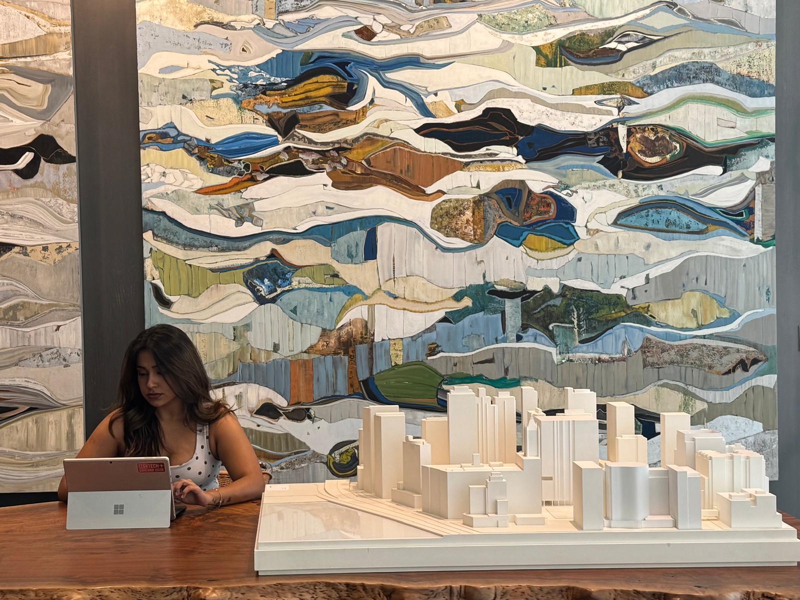 Bhavisha working on a laptop beside an architectural city model at the AEC Tech Hackathon, Gensler Chicago